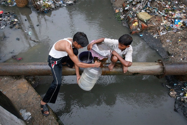 Two boys fill a container with drinking water from a leaking pipe over polluted water in Noida in the northern Indian state of Uttar Pradesh